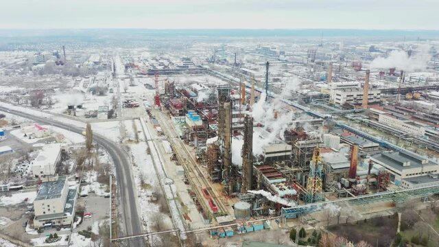 Massive nitrogen chemicals facility complex throwing smoke into sky. Obsolete soviet factory near road in the middle of Eastern European cityscape. Aerial view 4k UHD footage.  