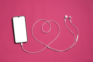 Top View, blank screen of new smartphone or mobile connected to earphones cable line shaped heart on pink background
