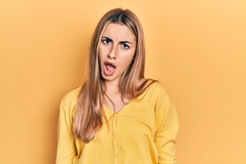 Beautiful hispanic woman wearing casual yellow sweater in shock face, looking skeptical and sarcastic, surprised with open mouth