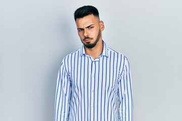 Young hispanic man with beard wearing casual striped shirt skeptic and nervous, frowning upset because of problem. negative person.