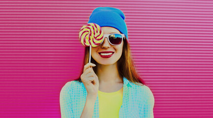 Portrait of smiling young woman with sweet colorful lollipop on pink background