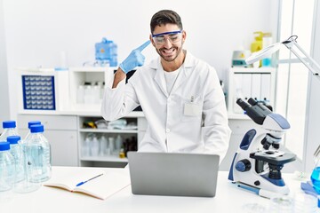 Fototapeta na wymiar Young hispanic man working at scientist laboratory with laptop smiling happy pointing with hand and finger