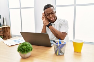 Young african man working at the office using computer laptop sleeping tired dreaming and posing with hands together while smiling with closed eyes.