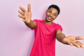 Young african american man wearing casua t shirt looking at the camera smiling with open arms for hug. cheerful expression embracing happiness.