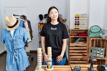 Young asian woman working as manager at retail boutique smiling looking to the side and staring...