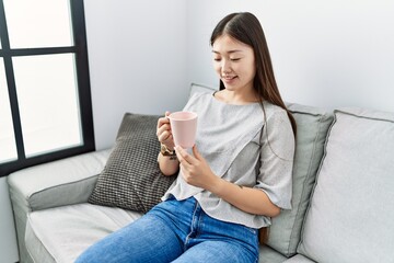 Young asian woman drinking cup of coffee sitting on the sofa at the living room