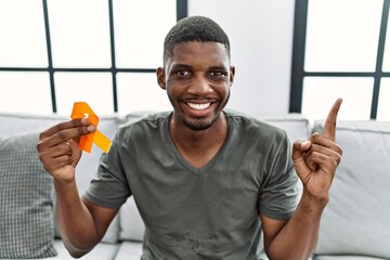 Young african american man holding awareness orange ribbon sitting on the sofa smiling happy...