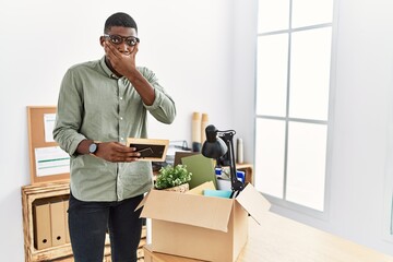 Young african american businessman unboxing box at the office shocked covering mouth with hands for mistake. secret concept.