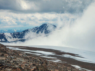 Storm on the top of a mountain. Wonderful dramatic landscape with big snowy mountain peaks above low clouds. Atmospheric large snow mountain tops in cloudy sky.