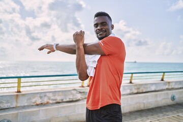 Young african american man wearing sportswear stretching at seaside
