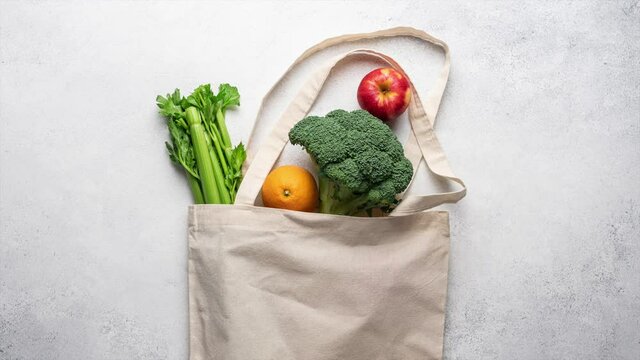 Stop motion animation of grocery shopping. Healthy vegetables and fruits putting in cotton bag on light background, top view