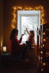 beautiful Christmas photo. Mom and daughter play on the windowsill in the light of Christmas lights.