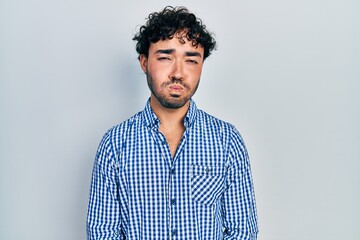 Obraz premium Young hispanic man wearing casual clothes puffing cheeks with funny face. mouth inflated with air, crazy expression.