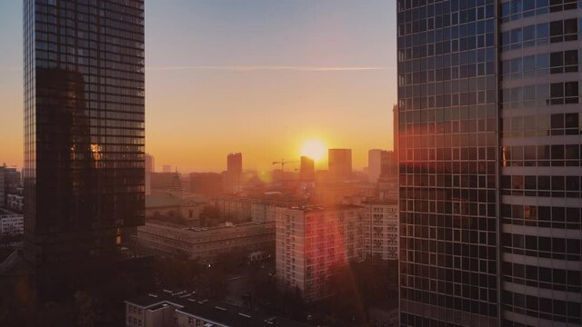 Modern business district city glass skyscrapers drone zoom in close to the buildings. Skyscraper in the big city top view during the sunrise when first sun rays are going through the glass windows.