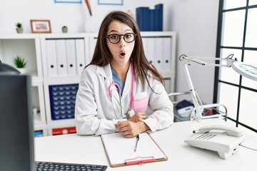 Obraz na płótnie Canvas Young doctor woman wearing doctor uniform and stethoscope at the clinic afraid and shocked with surprise expression, fear and excited face.