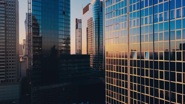 Modern business districtcity glass skyscrapers drone zoom in close to the buildings. Skyscraper in the big city top view during the sunrise when first sun rays are going through the glass windows.