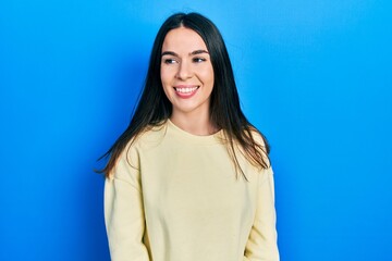 Fototapeta premium Young brunette woman wearing casual sweatshirt looking away to side with smile on face, natural expression. laughing confident.