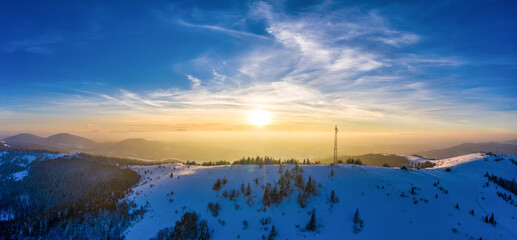 Flying over radio tower in mountains, snow covered winter landscape.