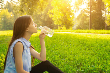 teenager summertime,young girl in the park drinks water,smiling,relaxes on a sunny summer day