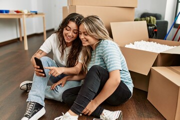 Young couple smiling happy using smartphone at new home.