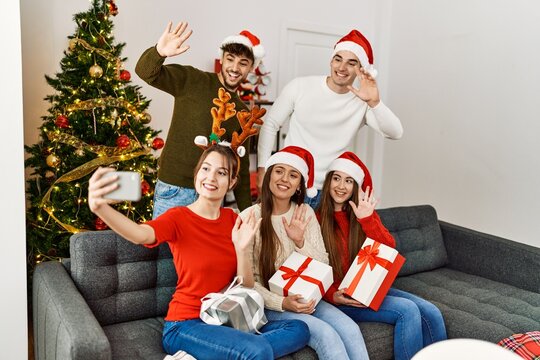 Group of young people holding christmas gifts make selfie by the smartphone at home.
