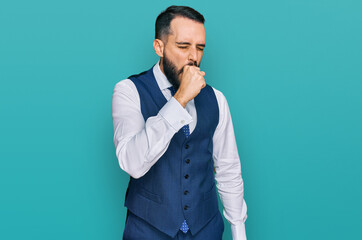 Young man with beard wearing business vest feeling unwell and coughing as symptom for cold or...