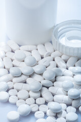 Closeup of white pills against white background with plastic pill container in the background with plastic pill container