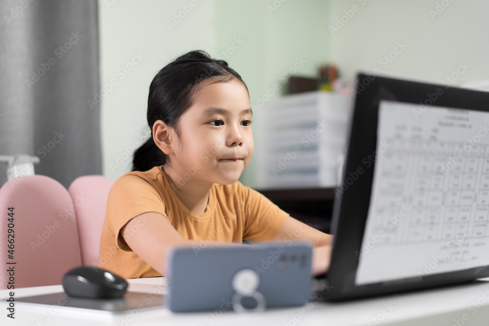 Wall mural asian child student or kid girl purse lips to enjoy diligent studying on computer laptop and smartph