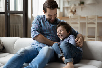 Affectionate loving young father tickling cute little preschool child son, relaxing together on...