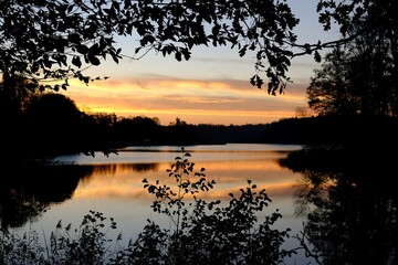 Beautiful scenery of sunrise over lake in frame with branches of trees.