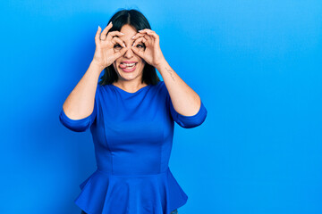 Young hispanic woman wearing casual clothes doing ok gesture like binoculars sticking tongue out, eyes looking through fingers. crazy expression.