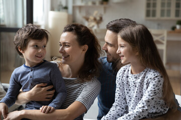 Obraz premium Happy friendly parents and small child girl listening to adorable little boy son, enjoying pleasant conversation together at home. Cheerful bonding family of four communicating, resting on weekend.