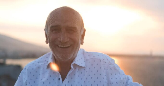Sympathetic old senior man's face portrait. Happy retired elderly guy is smiling to camera in afternoon time, with sun flare