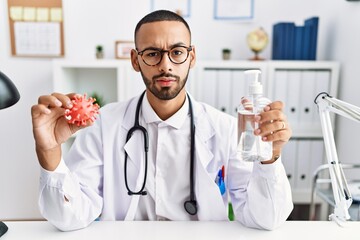 African american doctor man holding virus toy an sanitizer gel skeptic and nervous, frowning upset because of problem. negative person.