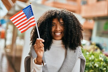 Young african american woman smiling happy holding United States flag at the city.