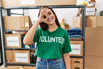 Young brunette woman wearing volunteer t shirt at donations stand doing ok gesture with hand...