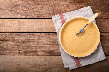 Dough for baking quiche, tart or pie in ceramic baking form ready for bake on kitchen towel over old rustic plank wooden background. Top view, copy space. Concept homemade baking for holiday.