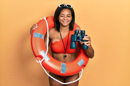 Young african american girl holding lifeguard floater using binoculars winking looking at the camera with sexy expression, cheerful and happy face.
