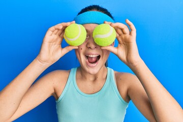 Beautiful brunette little girl holding tennis ball close to eyes celebrating crazy and amazed for...