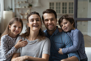 Portrait of smiling bonding affectionate family young parents and little adorable children siblings, happy married couple posing in modern living room with son and daughter, enjoying weekend pastime.