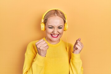 Young blonde woman listening to music using headphones excited for success with arms raised and eyes closed celebrating victory smiling. winner concept.