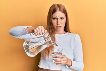 Young irish woman pouring water skeptic and nervous, frowning upset because of problem. negative...