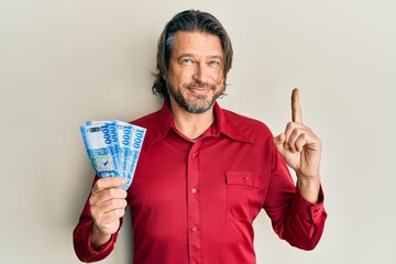 Middle age handsome man holding 1000 hungarian forint banknotes smiling with an idea or question pointing finger with happy face, number one