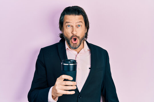 Middle age caucasian man wearing business clothes drinking a cup of coffee scared and amazed with open mouth for surprise, disbelief face