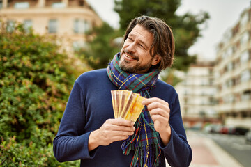 Middle age handsome man holding norwegian krone banknotes outdoors at the park