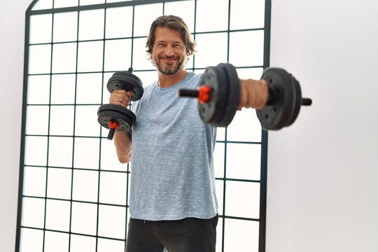 Middle age caucasian man smiling confident training using dumbbells at sport center