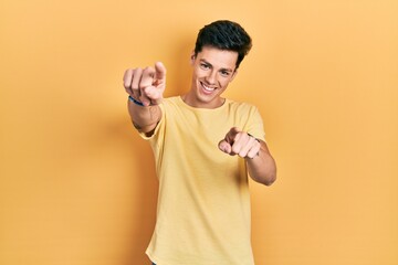 Young hispanic man wearing casual yellow t shirt pointing to you and the camera with fingers, smiling positive and cheerful