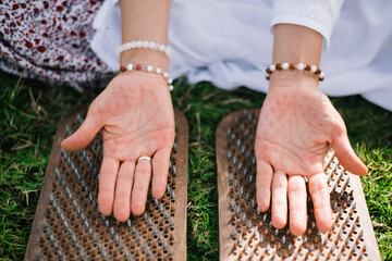 woman's hands visible mark from metal nails of wooden board for sadhu practice. Outdoor on green grass. Closeup.  Yoga for health, practice forgiveness. Sharp metal nails.