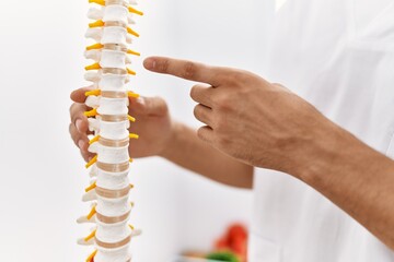 Young arab man wearing physiotherapist uniform pointing with finger to vertebral column at clinic