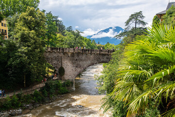 View of the famous Steinerner Steg - Ponte Romano bridge, a two-arched, stone-built footbridge across the Passer in Merano, South Tyrol, northern Italy. - obrazy, fototapety, plakaty